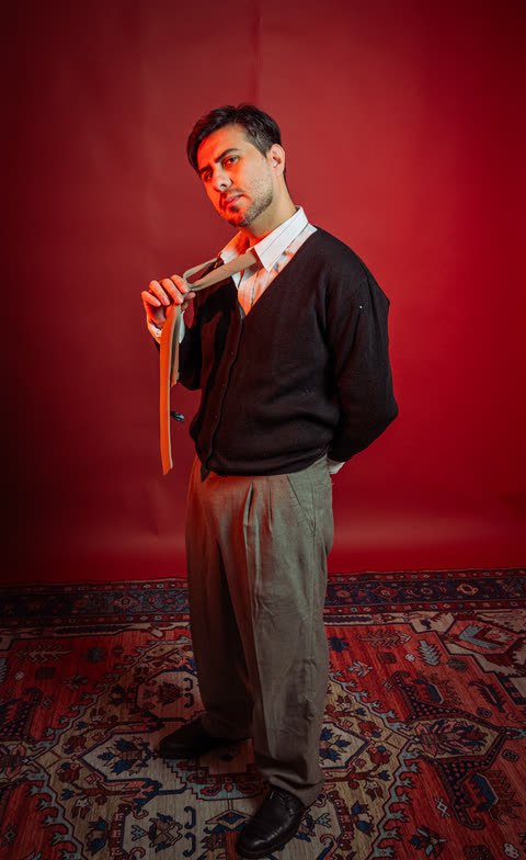 Diego Villalba, guitarrista de Planetas Errantes, sosteniendo una corbata frente a un fondo rojo